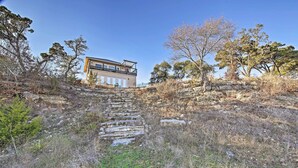 A modern house with a stone staircase leading up to a garage, surrounded by dry grass and trees. - Peaceful Hill Country Hideaway w/ Pond Views (Wimberley)
