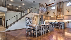A spacious kitchen with a central island, a dining area with multiple chairs, and a staircase leading to an upper level. - Kansas Hunting Lodge: Pets & Large Groups Welcome! (Great Bend)