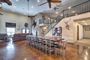A spacious living area with a high ceiling, a dining table with chairs, a staircase, and mounted animal heads on the walls. - Kansas Hunting Lodge: Pets & Large Groups Welcome! (Great Bend)