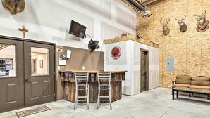 A kitchen with a bar area, a television mounted on the wall, and a wooden wall with mounted animal heads. - Kansas Hunting Lodge: Pets & Large Groups Welcome! (Great Bend)