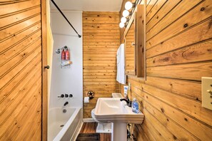 A wooden-paneled bathroom with a bathtub, sink, and mirror. - Pet-friendly Cody Home - Walk to Main Street! (Cody)