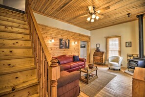 A wooden interior with a staircase, a red leather sofa, a white armchair, and a wood-burning stove. - Pet-friendly Cody Home - Walk to Main Street! (Cody)