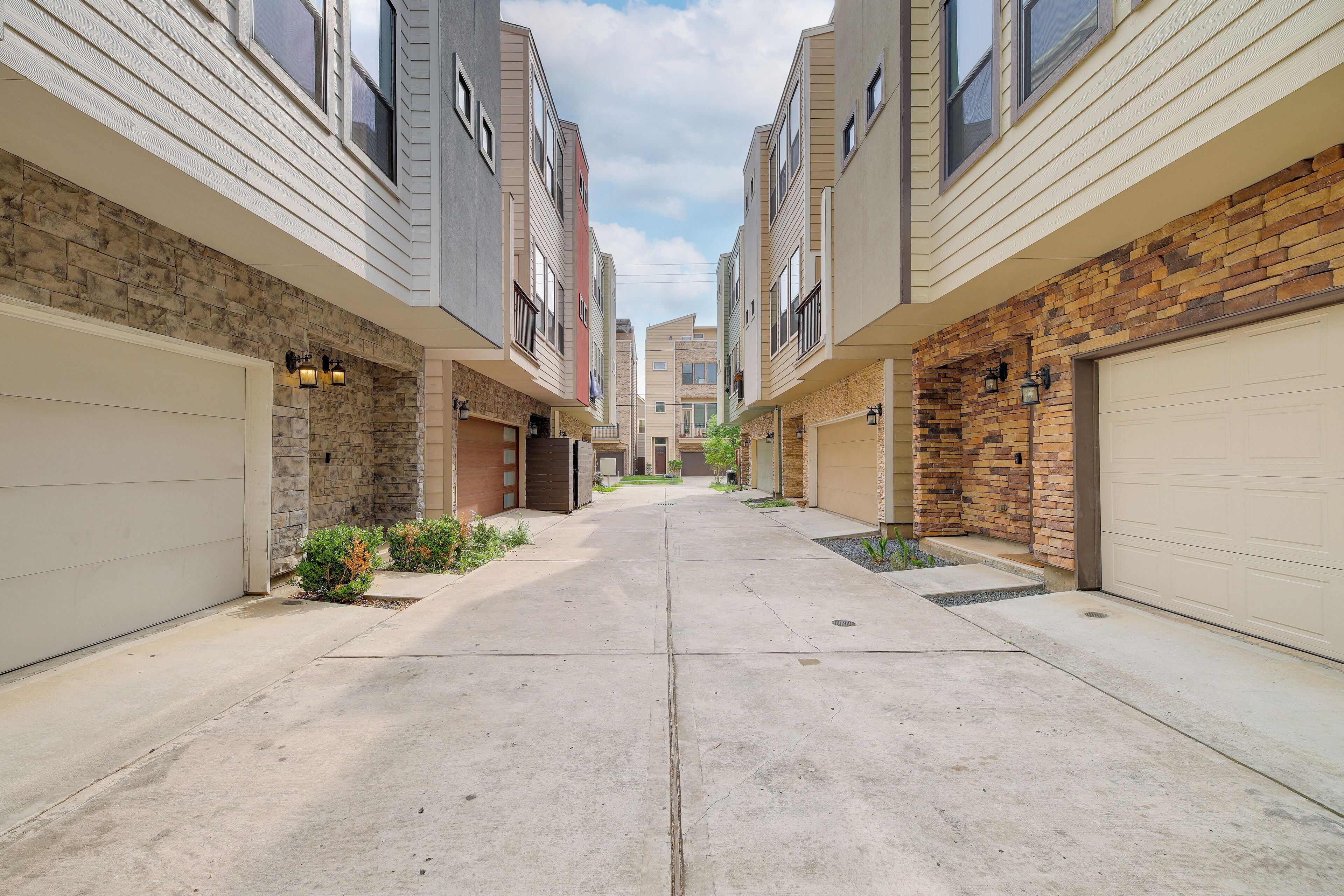A residential street with two-story houses, each with a garage door, a small front yard, and a stone facade.