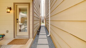 A narrow pathway leading to a door with a glass panel, flanked by wooden siding and a light fixture. - Houston Vacation Rental ~ 1 Mi to Downtown! (Houston)