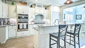 A modern kitchen with white cabinetry, a built-in oven, a backsplash, and a bar area with stools. - North Augusta Getaway w/ Large Deck & Yard (North Augusta)