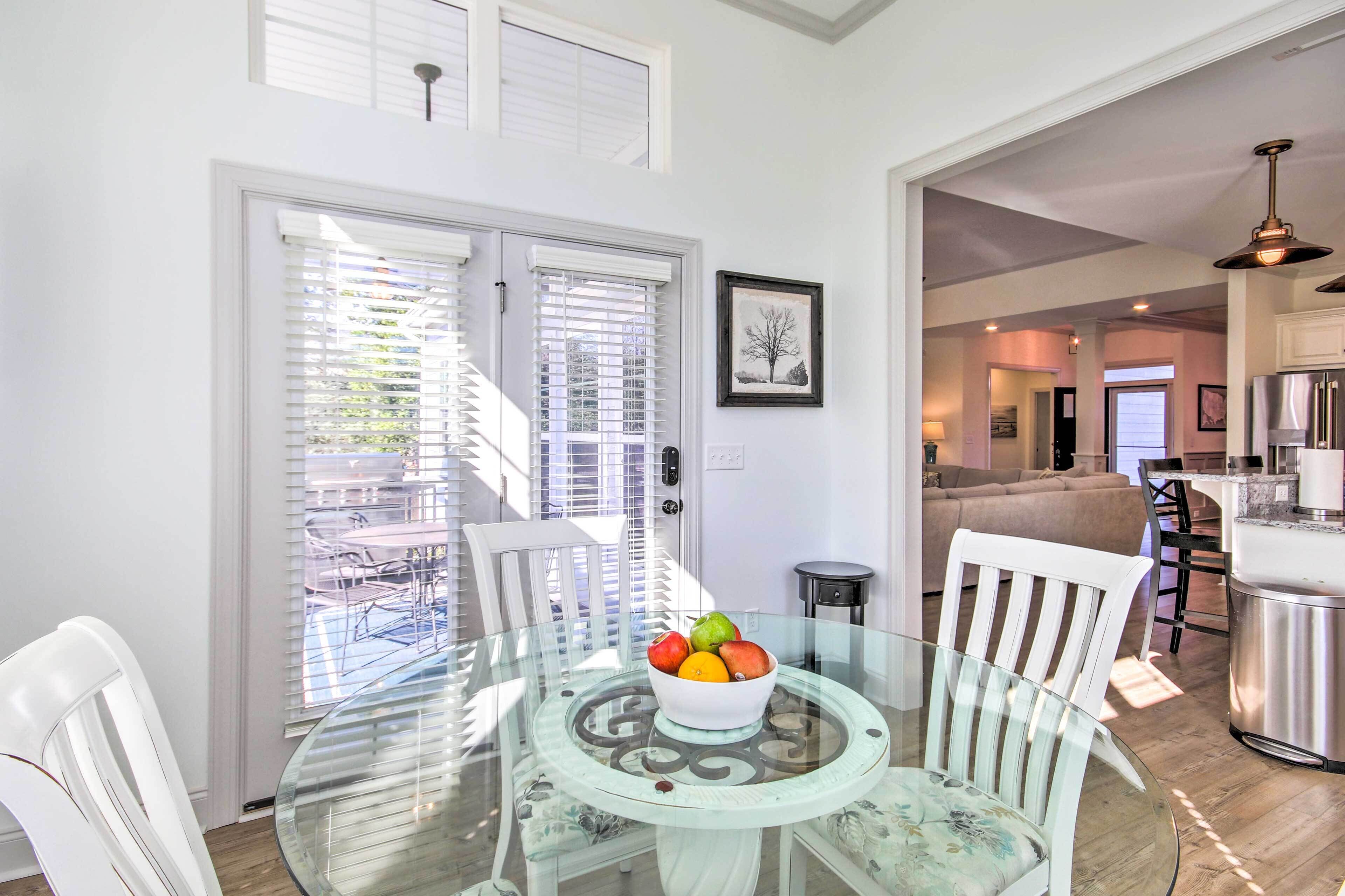 A dining area with a glass table, white chairs, and a bowl of fruit.