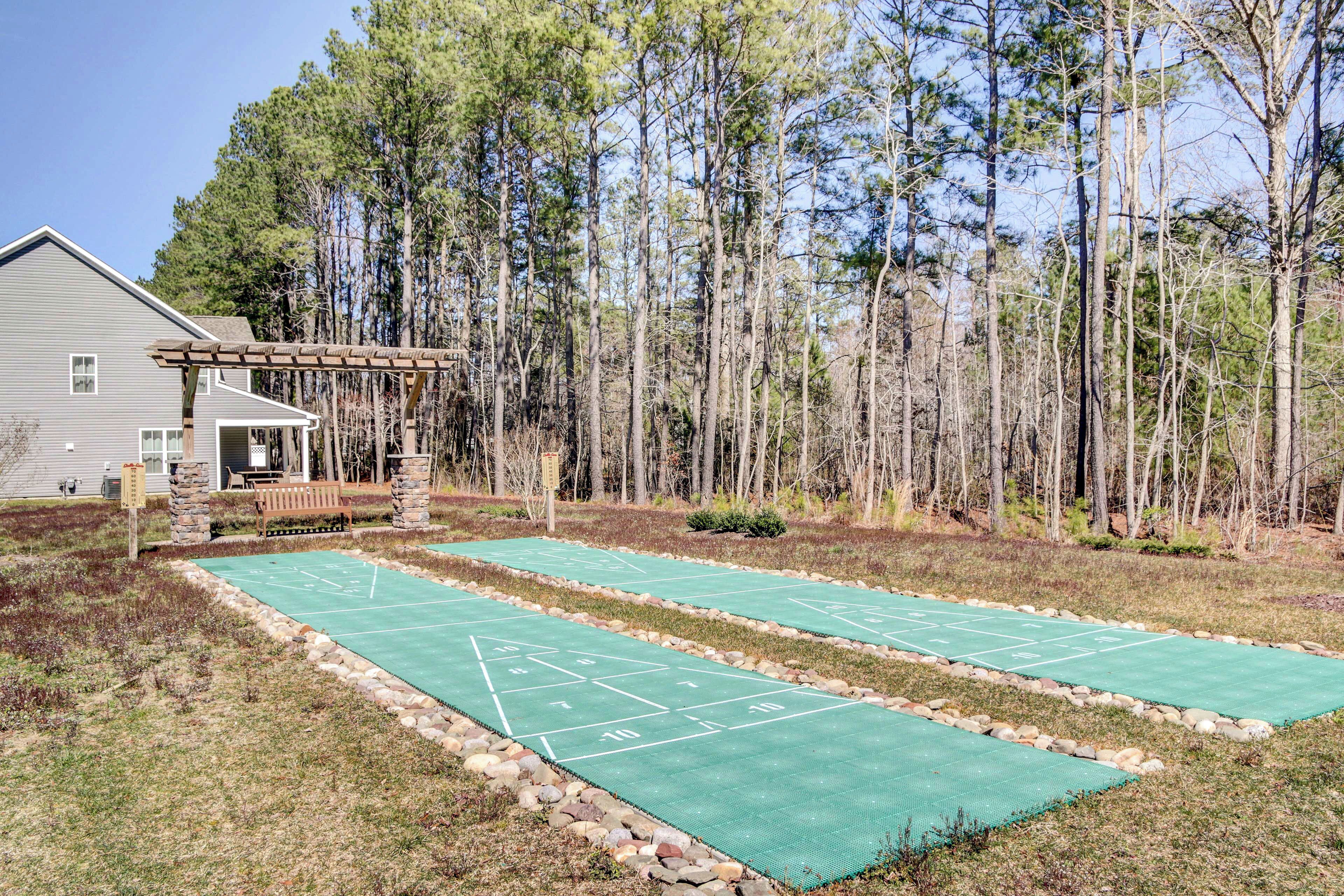 A courtyard with two shuffleboard courts, a wooden pergola, and a stone wall.
