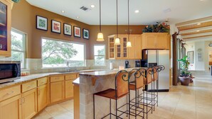 A modern kitchen with a central island, bar stools, wooden cabinets, and pendant lighting. - Luxe Lake Travis Vacation Rental w/ Heated Pool (Leander)