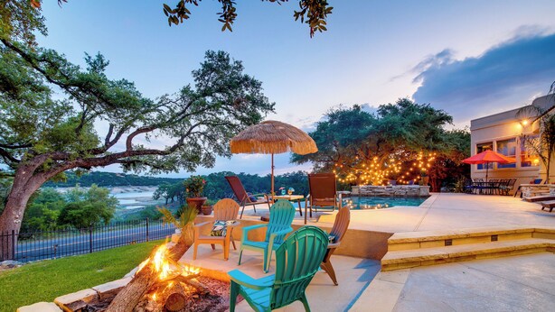 An outdoor patio with a fire pit, chairs, and an umbrella. - Luxe Lake Travis Vacation Rental w/ Heated Pool (Leander)
