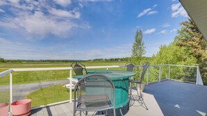 A deck with a table and chairs, overlooking a grassy field and a distant landscape.