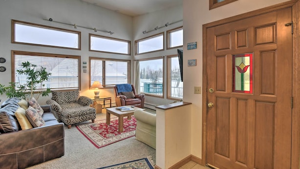 A living room with a sofa, armchair, and coffee table, large windows, and a wooden door.