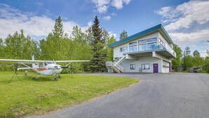A modern two-story building with a glass balcony, a small airplane parked in front, and a clear sky.