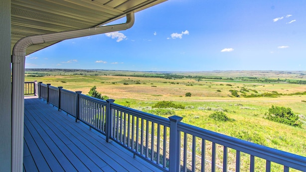 A wooden deck with a railing overlooking a grassy landscape. - Sunny Big Timber Retreat w/ Spacious Deck! (Big Timber)