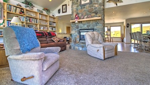A cozy living room with a stone fireplace, a bookshelf filled with books, and a comfortable seating area with a blue blanket. - Sunny Big Timber Retreat w/ Spacious Deck! (Big Timber)