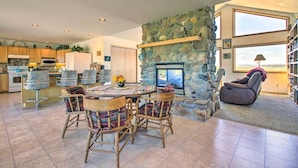 A spacious kitchen with modern appliances, a stone fireplace, and a dining area with wicker chairs. - Sunny Big Timber Retreat w/ Spacious Deck! (Big Timber)