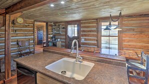 A rustic kitchen with a granite countertop, stainless steel sink, and wooden walls. - Rustic & Rural Cabin in Dupuyer on Open 14 Acres! (Dupuyer)