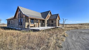 A log cabin with a porch and a bench, surrounded by dry grass and a dirt road. - Rustic & Rural Cabin in Dupuyer on Open 14 Acres! (Dupuyer)
