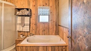 A wooden-paneled bathroom with a freestanding bathtub, a towel rack with towels, and a window with patterned curtains.