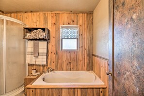 A wooden-paneled bathroom with a freestanding bathtub, a towel rack with towels, and a window with patterned curtains.