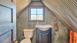 A bathroom with a sloped ceiling, a window, a toilet, and a sink with cabinets.