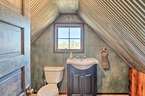 A bathroom with a sloped ceiling, a window, a toilet, and a sink with cabinets.