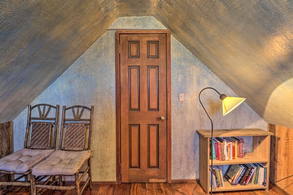 Una habitación cálida en el ático con puerta de madera, dos sillas de madera, una pequeña estantería y un escritorio.