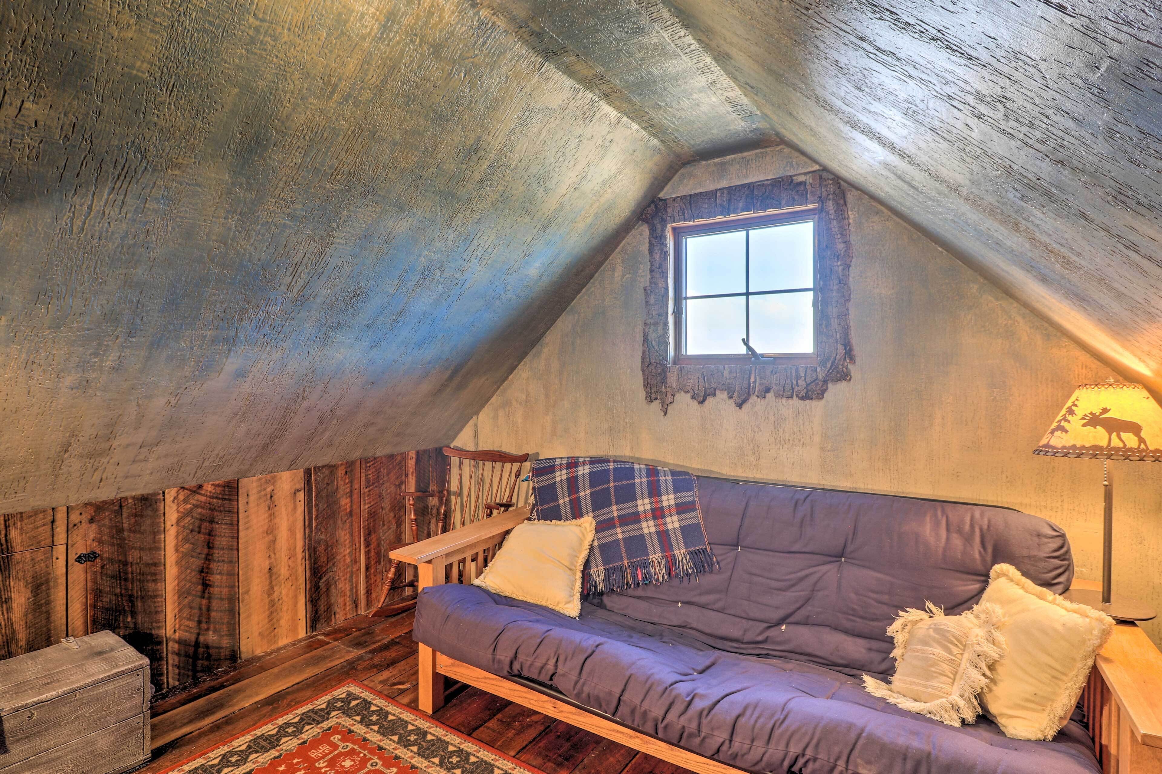 Acogedor dormitorio en el ático con suelo de madera, un sofá púrpura, una mesita y una ventana con vistas.