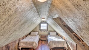 A cozy attic bedroom with two beds, a small window, and a wooden floor.