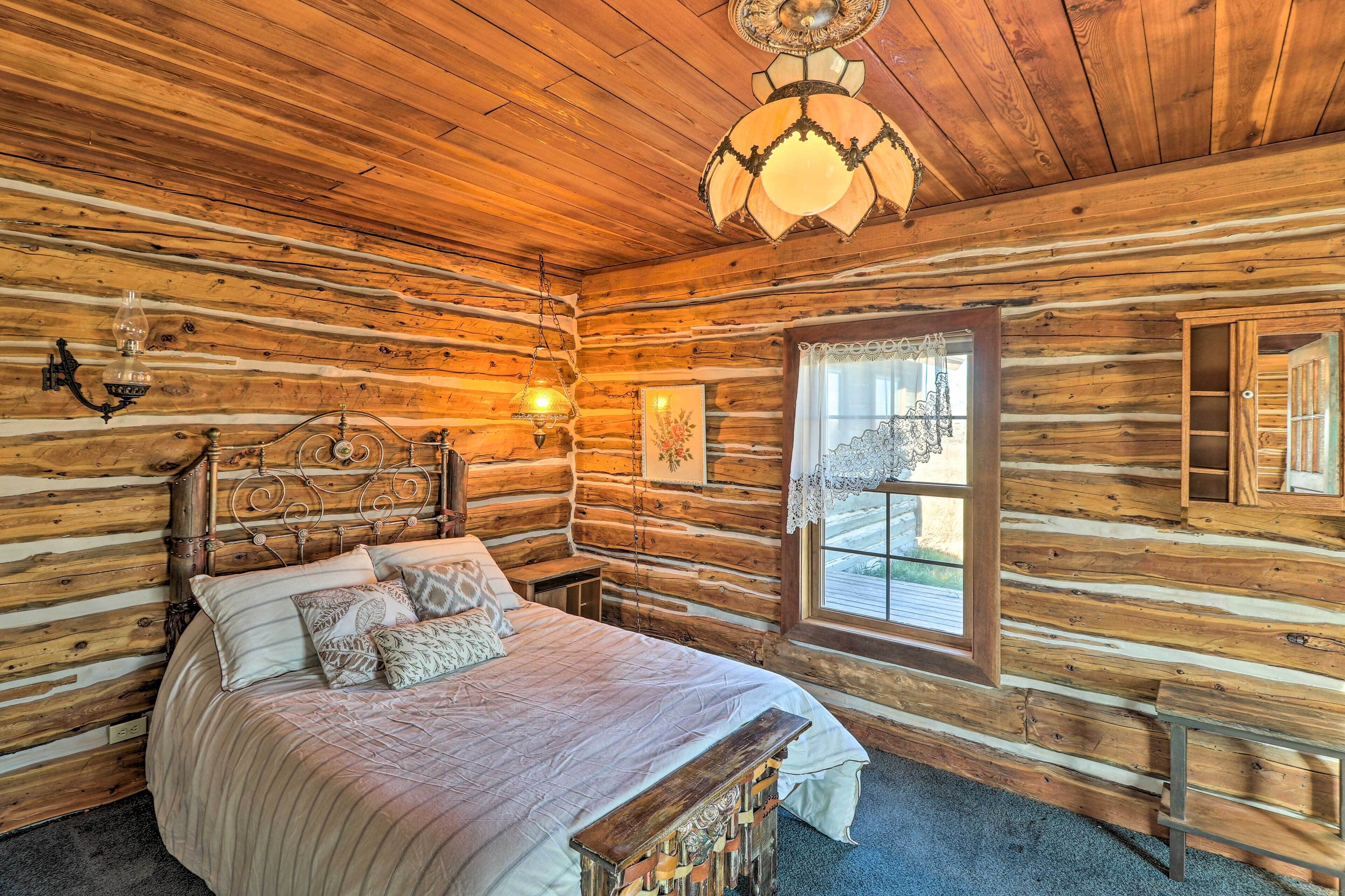 Ein Schlafzimmer in einer Blockhütte mit einem hölzernen Bett, einer Pendelleuchte und einem Fenster mit Blick.