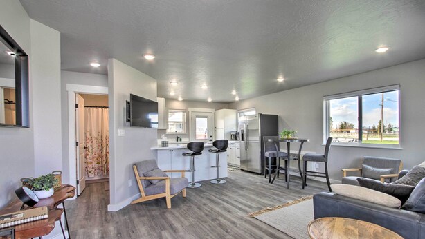 Una sala de estar moderna con un sofá gris, una mesa de centro de madera y una zona de cocina con un refrigerador y taburetes de bar.