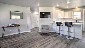 Una cocina moderna con armarios blancos, una barra con taburetes y una silla tapizada en gris.