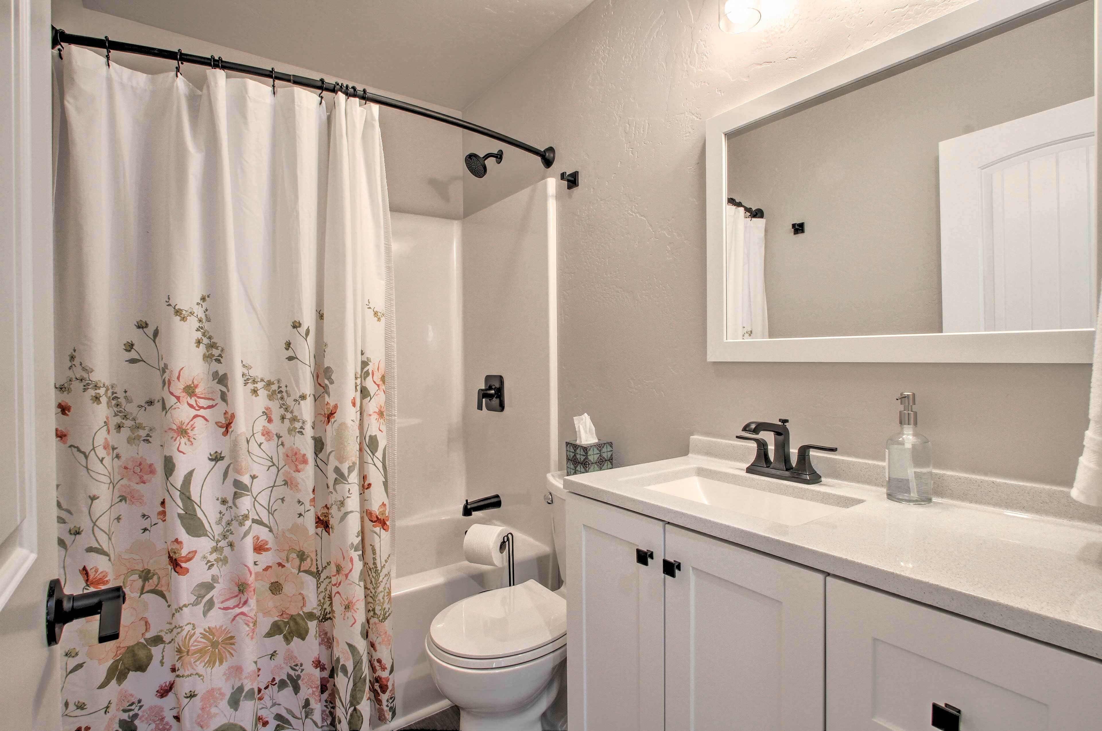 A bathroom with a shower curtain, toilet, sink, and cabinet.