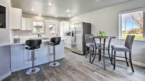 Una cocina moderna con gabinetes blancos, un refrigerador de acero inoxidable y una zona de comedor con dos taburetes altos y una mesa.