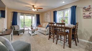 A spacious living room with a dining area, large windows with blue curtains, a ceiling fan, and artwork on the walls.