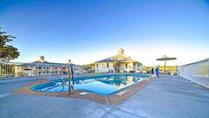 A swimming pool with a surrounding deck, a lifeguard stand, and a building with a distinctive roof in the background.