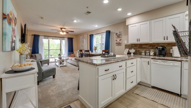 A modern kitchen with white cabinetry, a central island, and a dining area with a sofa and chairs.