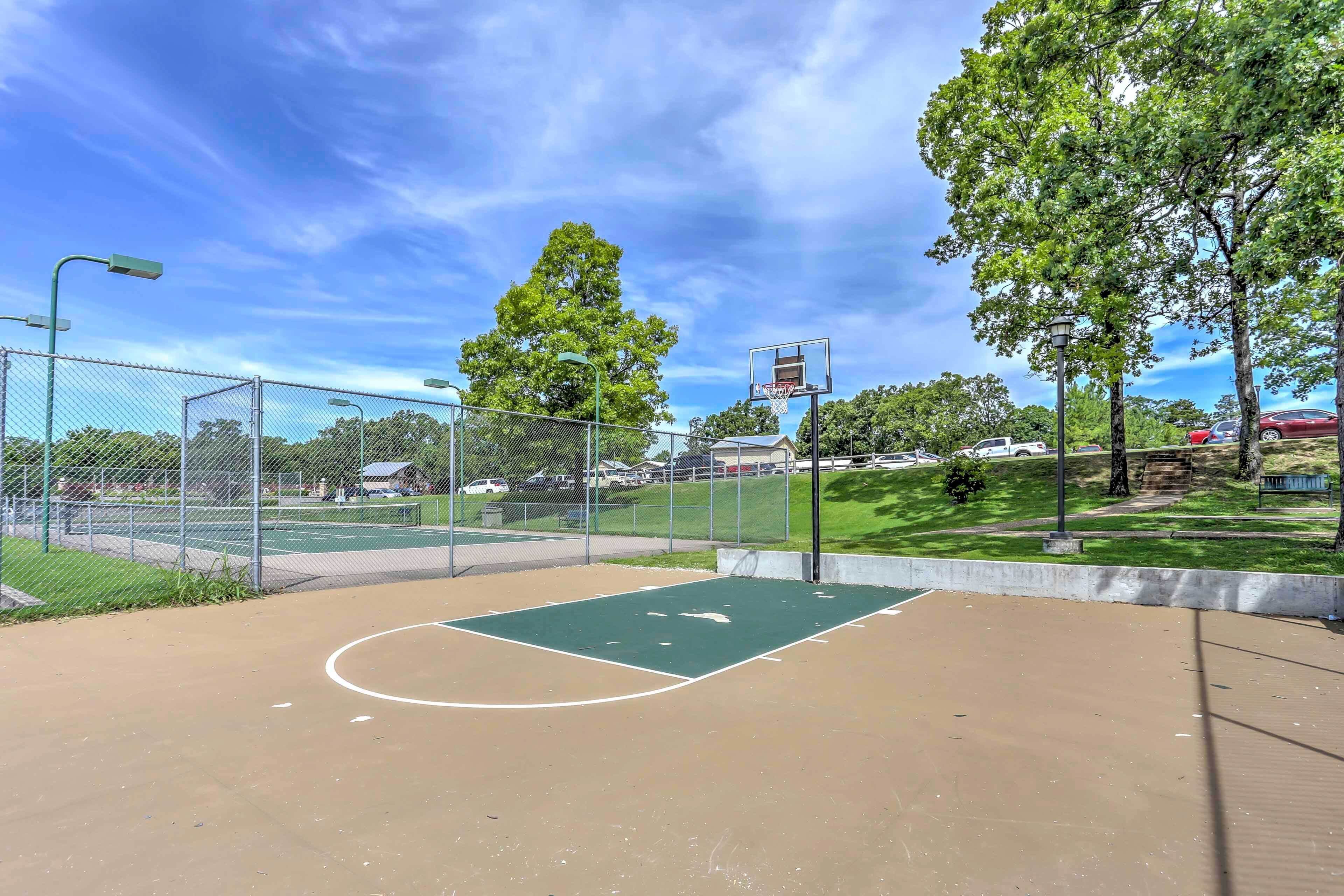 An outdoor basketball court with a chain-link fence, trees, and a clear sky.