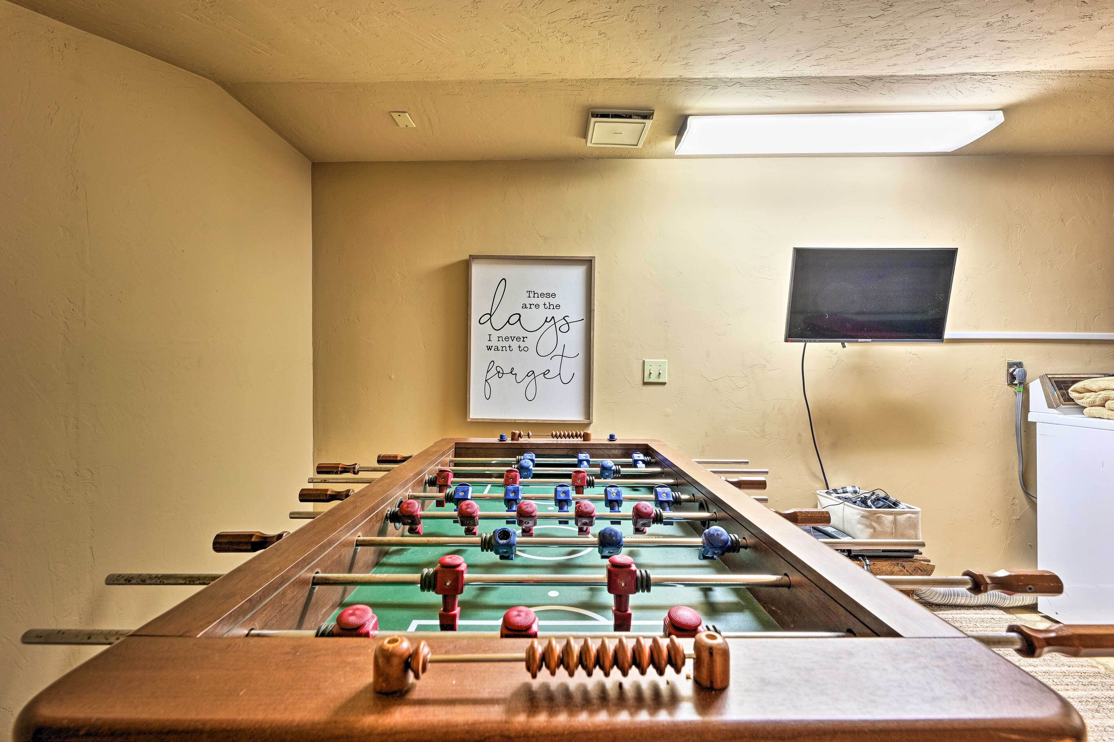 Una mesa de fútbol de mesa en una habitación con paredes color beige, una cita inspiradora enmarcada y un televisor montado en la pared.