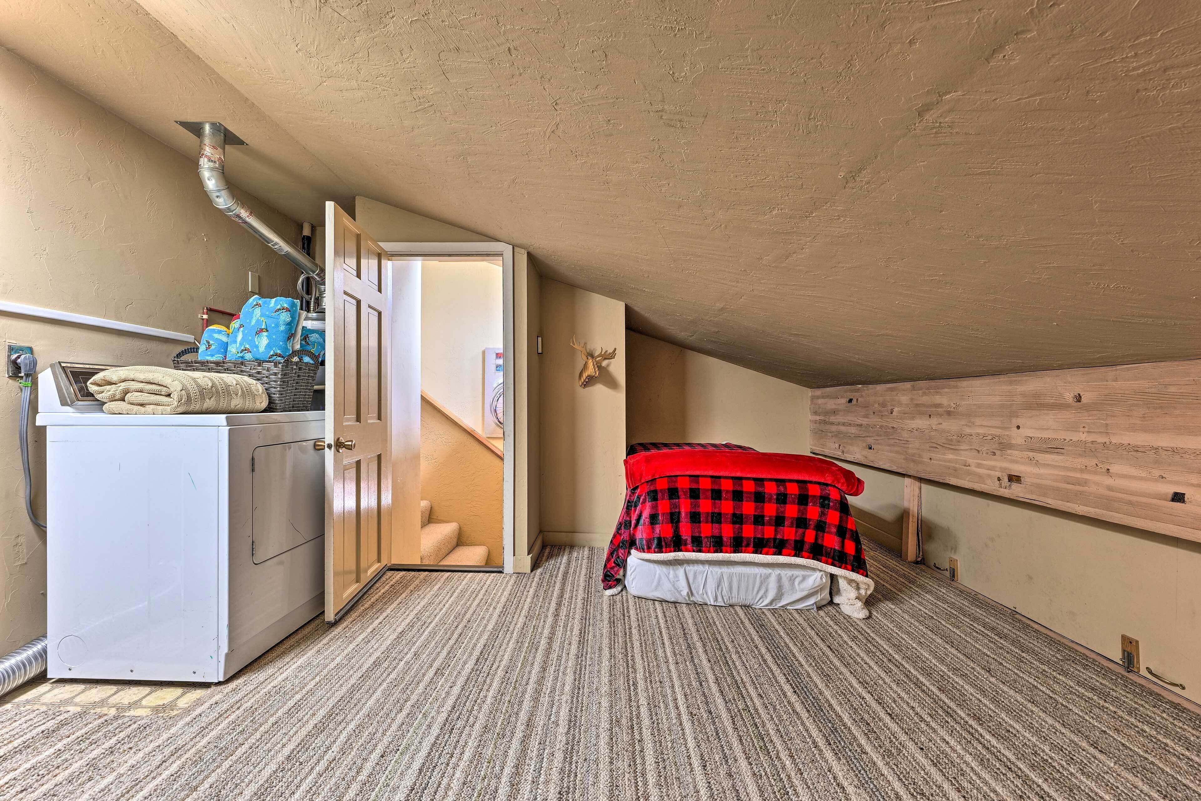 A compact room with a washing machine, a bed with a red and black checkered blanket, and a wooden wall.