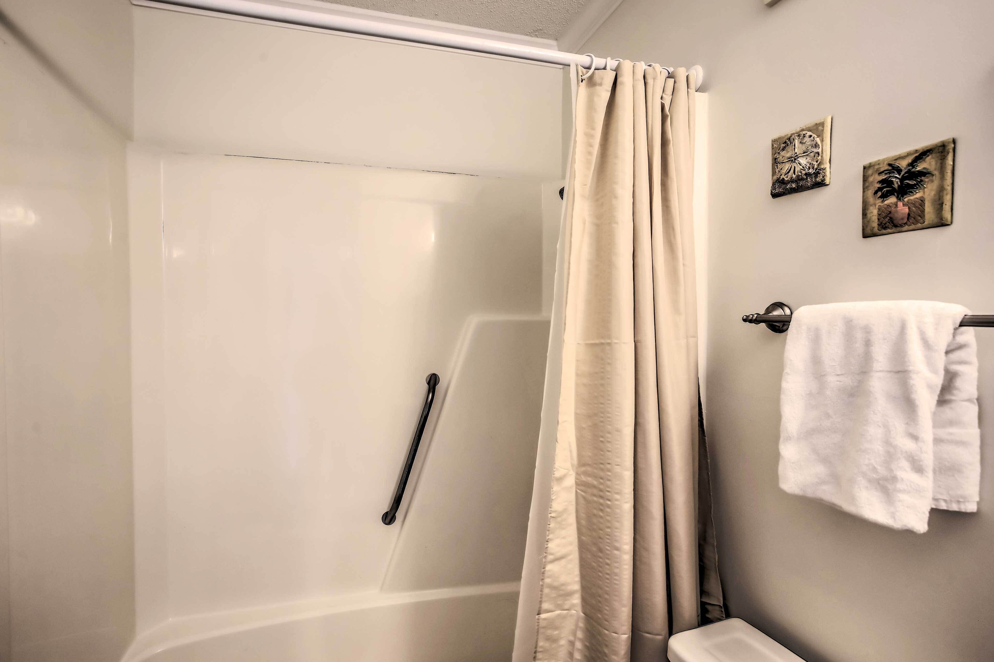 Ett badrum med en duschavdelning med glasväggar, en beige duschdraperi, en handduksställning med ett vitt handduk och två tavlor som hänger på väggen.