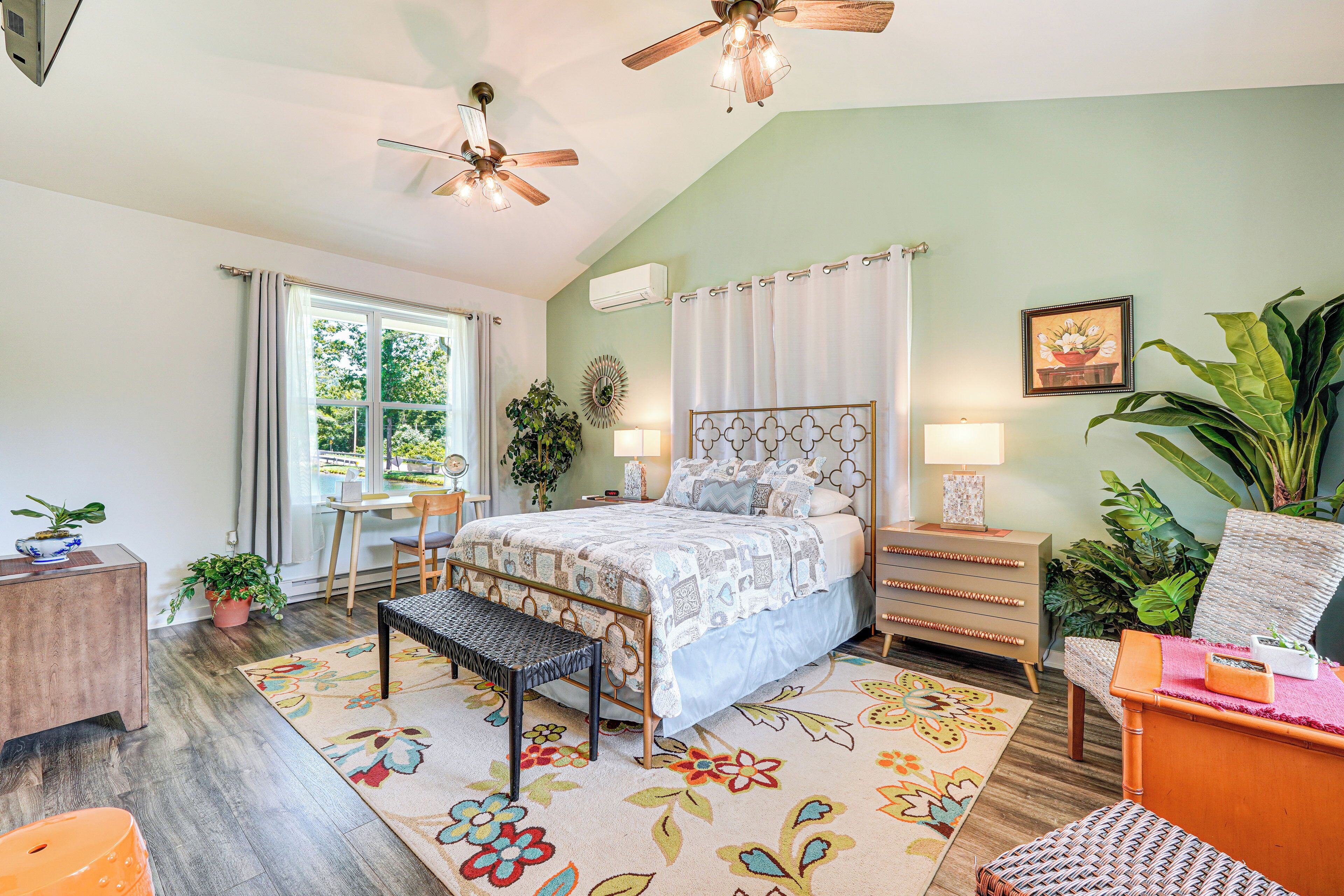 A bedroom with a bed, bedside tables, a bench, a desk, and a window with curtains.
