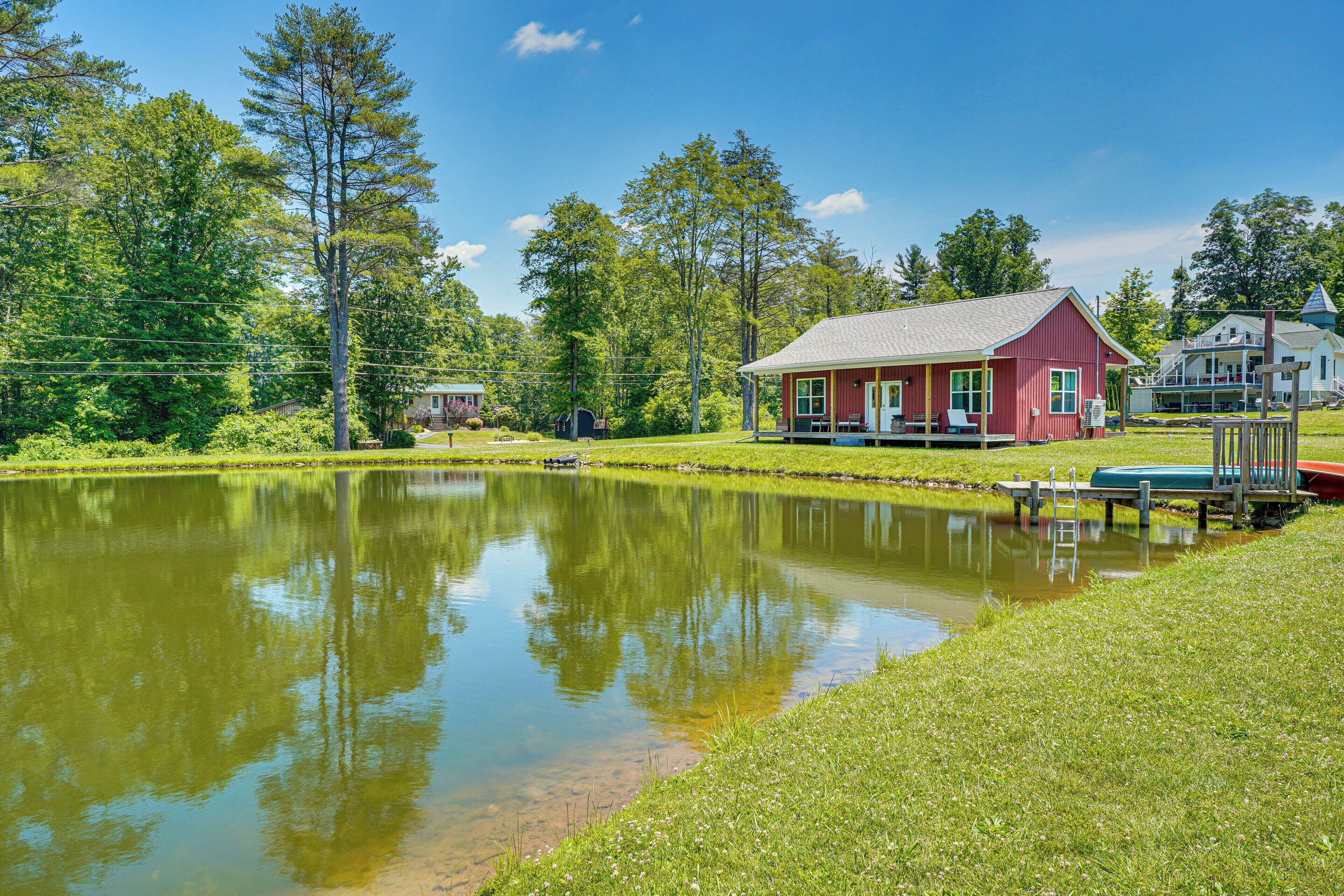 A red building with a porch, a pond, and surrounding greenery.