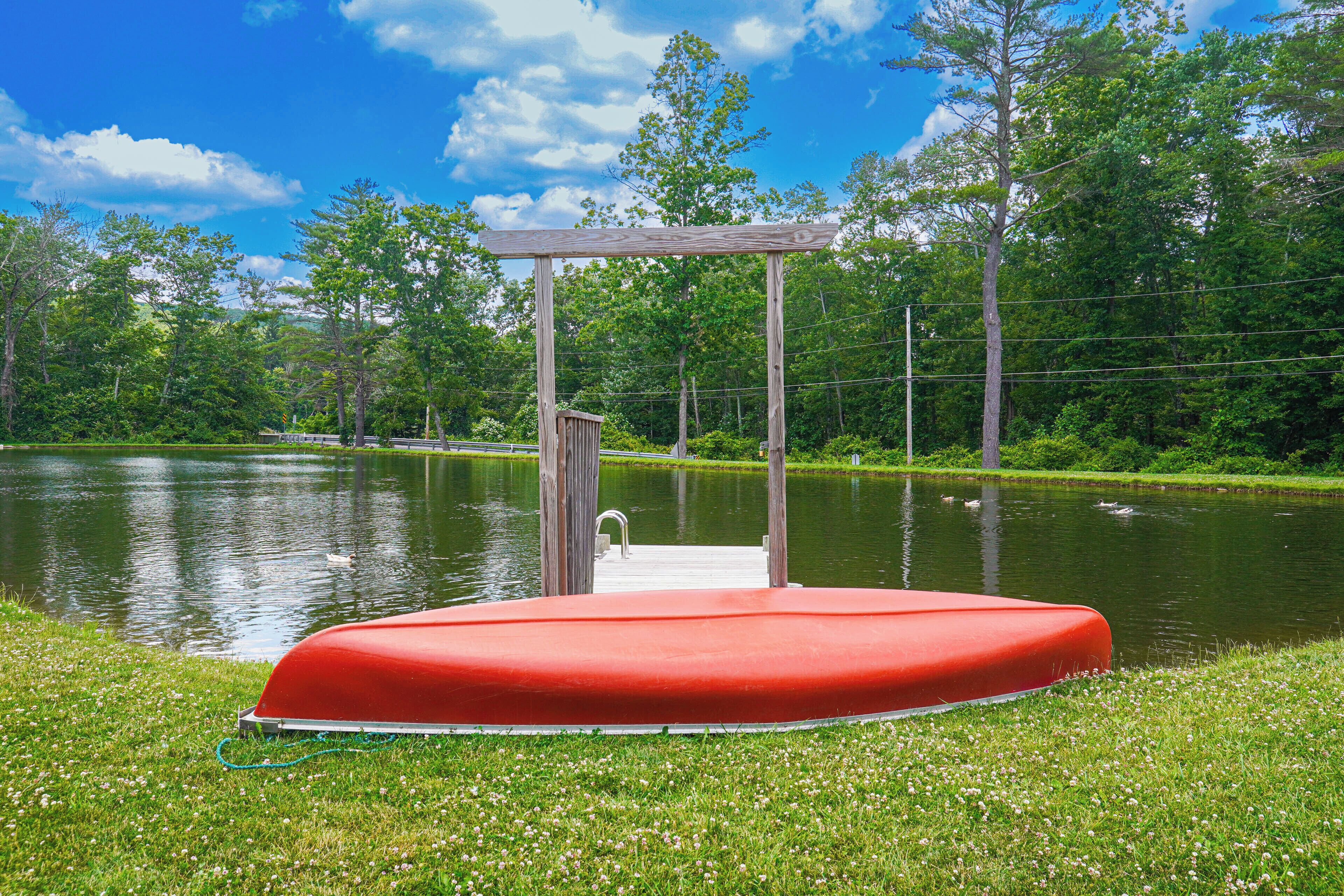 A red floating platform with a wooden pergola structure, surrounded by a grassy area and a body of water.