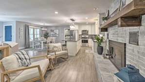 A modern kitchen with a stone fireplace, wooden shelves, and a dining area with a view to the outdoors.