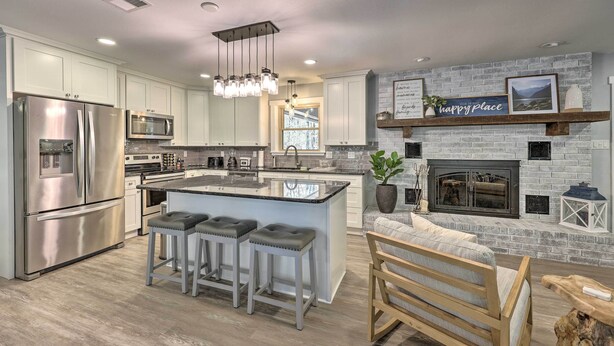 A modern kitchen with stainless steel appliances, a central island with bar stools, a fireplace, and a view of the outdoors.