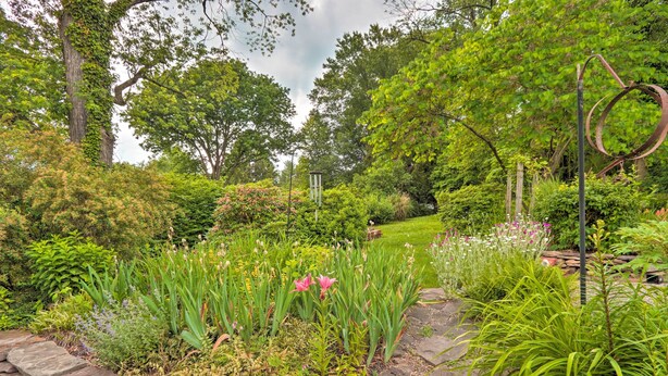 A lush garden with a variety of plants and flowers, a stone wall, and a metal sculpture. - Charming Abode w/ Patio - Walk to Town + River! (Stockton)