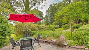 An outdoor patio with a table and chairs, a red umbrella, and a garden with various plants and a stone pathway. - Charming Abode w/ Patio - Walk to Town + River! (Stockton)