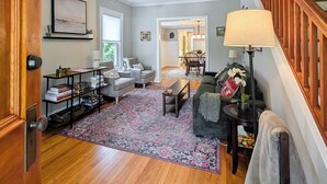 A living room with a sofa, a coffee table, a bookshelf, a rug, and a staircase. - Charming Abode w/ Patio - Walk to Town + River! (Stockton)