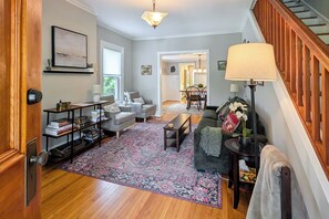 A living room with a sofa, a coffee table, a bookshelf, a rug, and a staircase. - Charming Abode w/ Patio - Walk to Town + River! (Stockton)