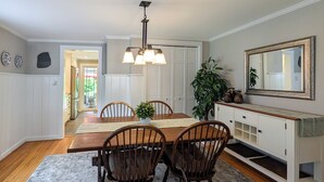 A dining room with a wooden table, four chairs, a chandelier, a large mirror, and a plant. - Charming Abode w/ Patio - Walk to Town + River! (Stockton)